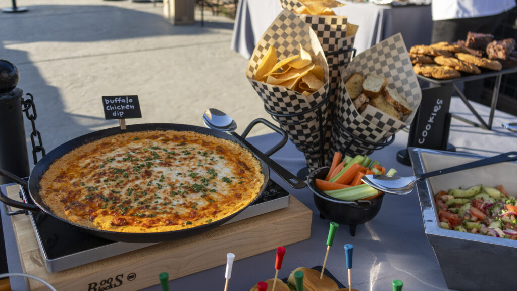 Buffalo chicken dip appetizer station with tortilla chips, crostini, fresh vegetables, cookies, brownies, sliders, and salad served as part of a catered event buffet.