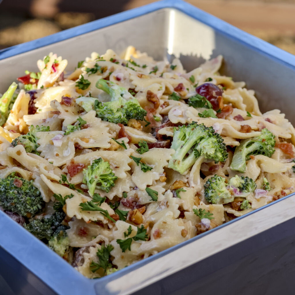 Broccoli bowtie pasta salad with bacon, red grapes, red onion, walnuts, and creamy dressing served as a catering side dish for weddings, corporate events, and golf outings.