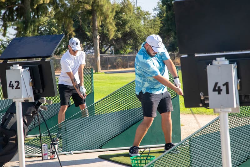 Two golfers practicing their swings from individual hitting bays at The Hangout driving range at Haggin Oaks Golf Complex in Sacramento.